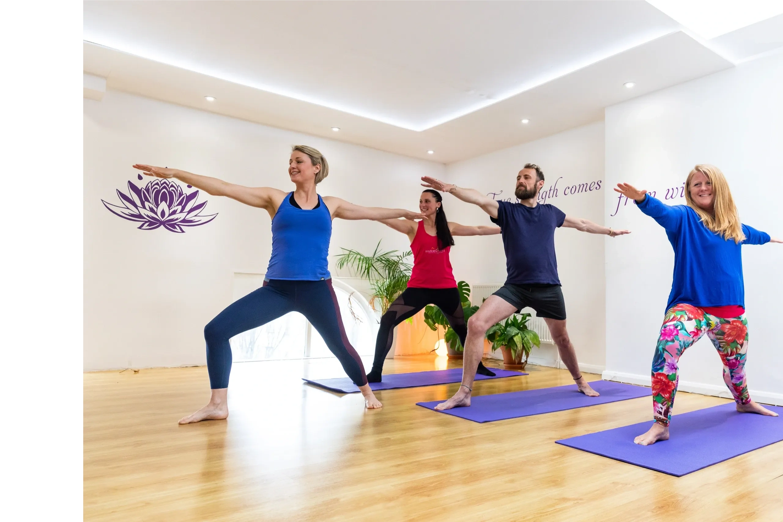 Four White adults in Warrior II pose Virabhadrasana II in Yoga Studio on purple yoga mats