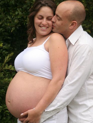 Pregnant woman hugged and kissed by a man outdoors.
