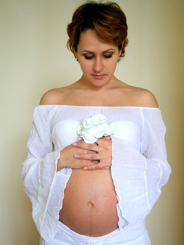 Pregnant woman holding a white flower, looking down.