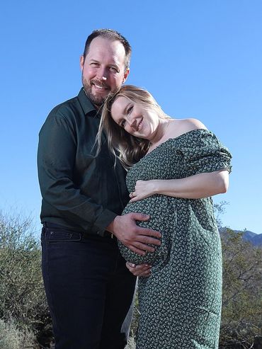 Pregnant woman and man smiling outdoors under clear sky.