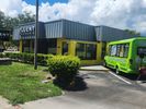 Green tourist train parked beside a modern building under a blue sky.