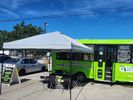 Green bus with a white canopy and a dog outside on a sunny day.
