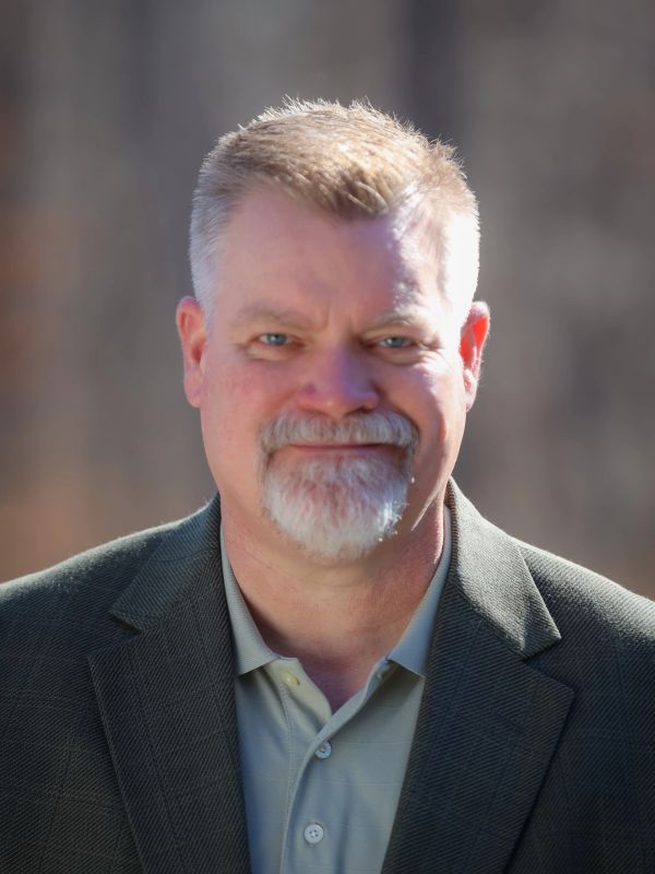 Middle-aged man with gray beard in suit jacket.