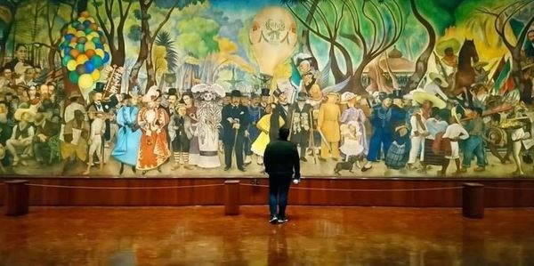 A person admires a vibrant, detailed mural in an art gallery.