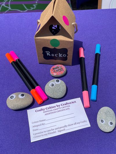 Crafted pet rocks with googly eyes, markers, and an adoption certificate on a purple surface.
