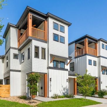 Modern white townhouses with wooden balconies and green landscaping under a clear blue sky.