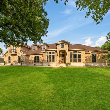 Spacious stone house with large windows and lush green lawn under a clear blue sky.