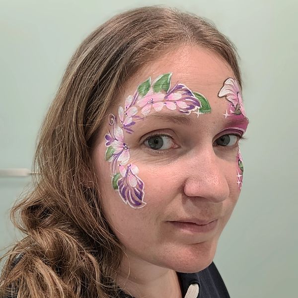 girl with white pink and purple flowers painted around her right eye long island facepai