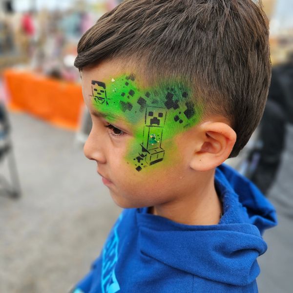 Little boy with black and green neon minecraft facepaint on side of his face