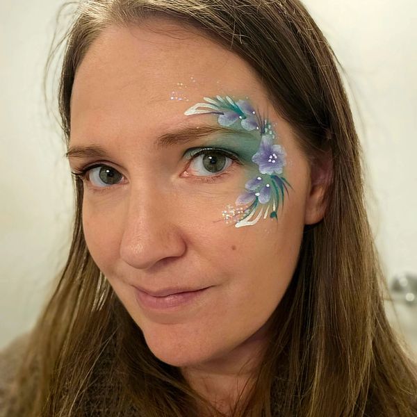  girl with white green and purple flowers painted around her eye. By long island facepainter
