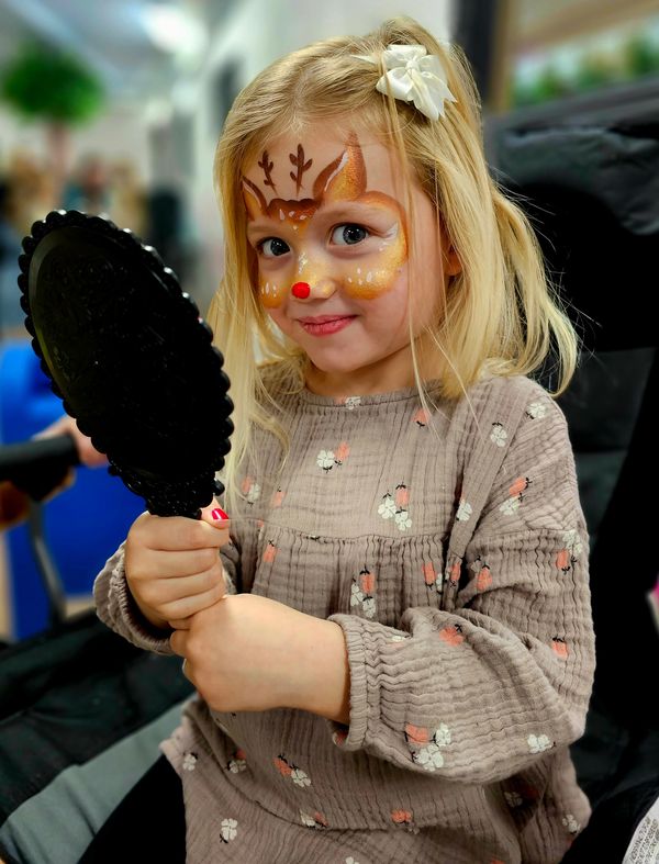 Little girl looking in the mirror with reindeer facepaint design on her face