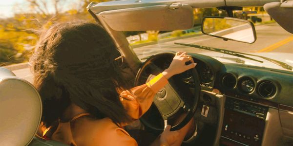 A female CEO celebrating career success driving her car on the open road in the sunshine. PR leaders