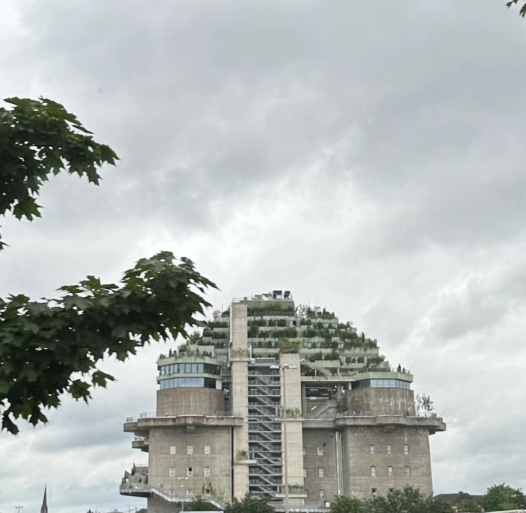 Modern concrete building with tiered rooftop garden under cloudy sky.