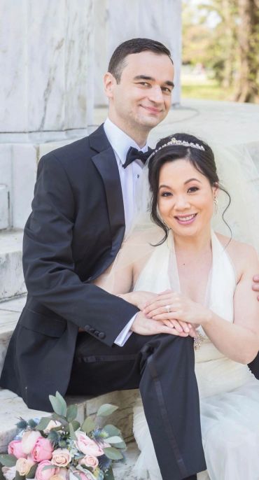 A happy bride and groom sitting outdoors, smiling at the camera.