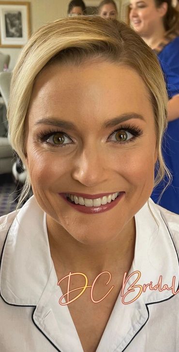 Smiling woman in bridal makeup and white robe.
