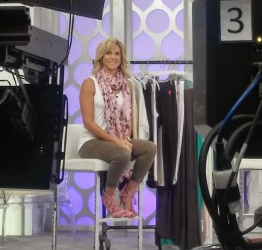 Woman posing on a chair in a studio with clothes hanging.
