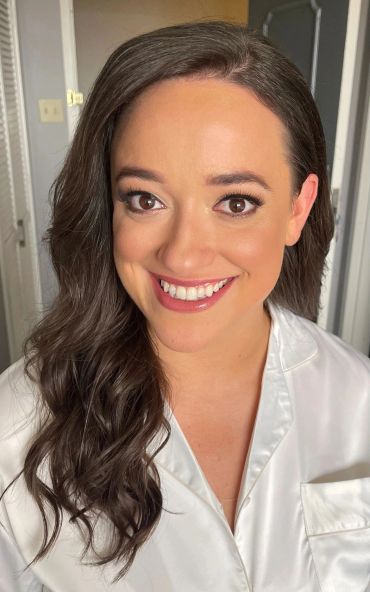 Smiling woman with long dark hair in a white shirt.