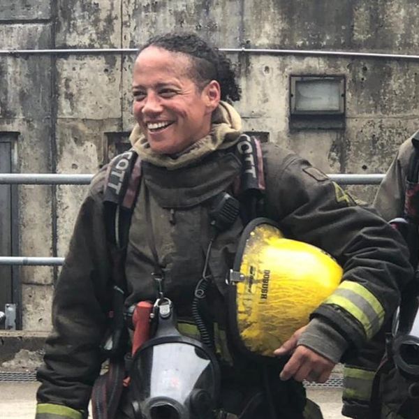 Smiling firefighter in full gear holding a yellow helmet.