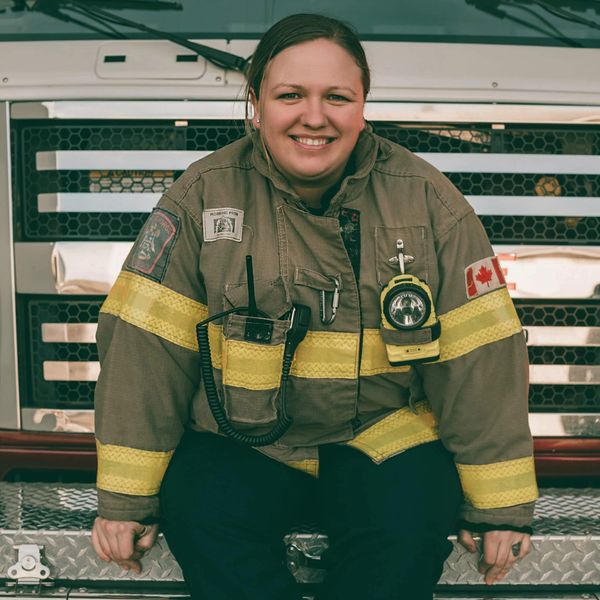 Smiling female firefighter in uniform sitting on a fire truck.