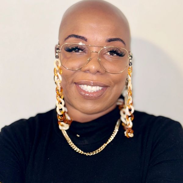 Smiling bald woman with stylish glasses and bold accessories.