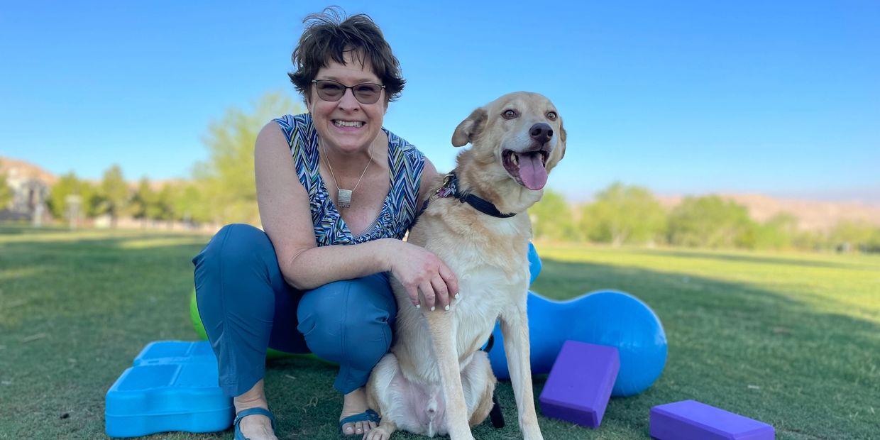 Woman smiling with her dog on a grass field surrounded by yoga props.