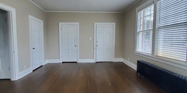 Empty room with three white doors and large windows.