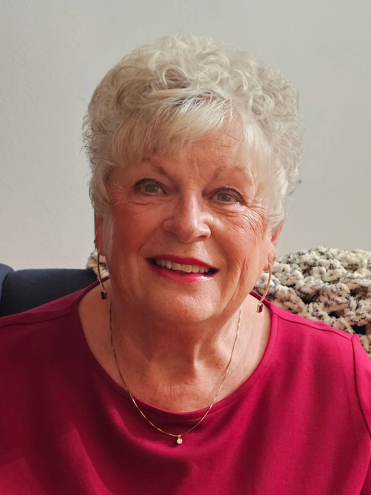 Smiling elderly woman with curly white hair and a red top.
