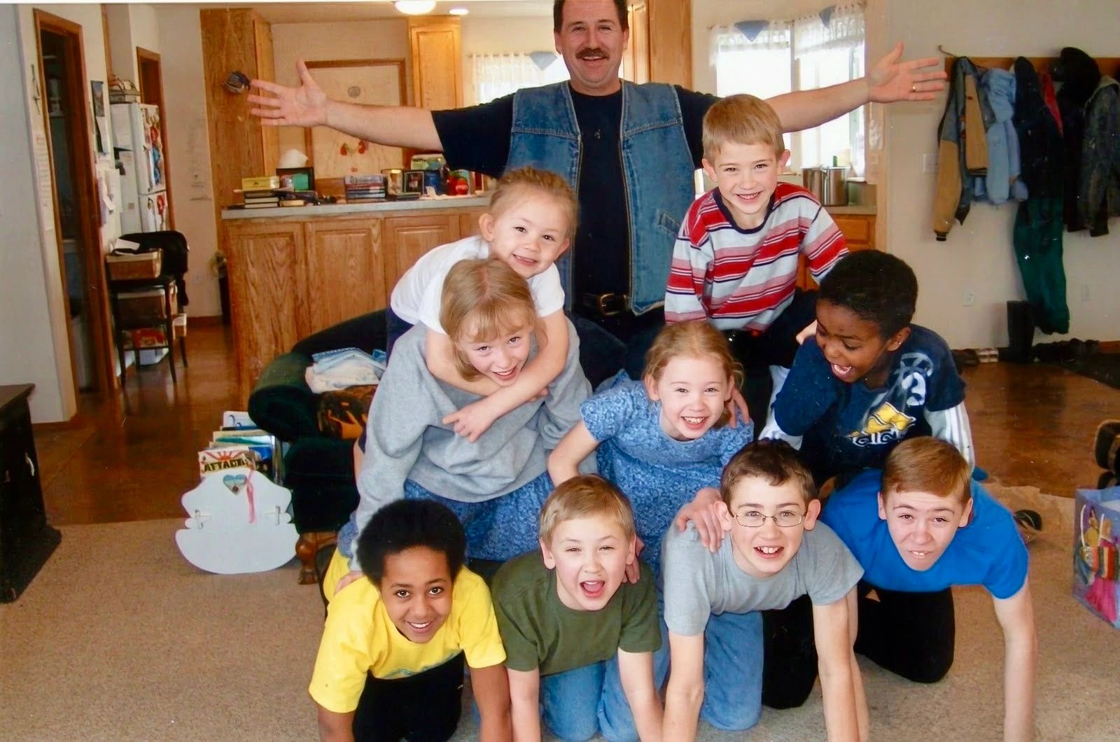 Man and kids in a playful human pyramid indoors.
