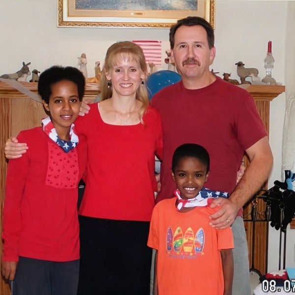 Family portrait with two adults and two children smiling indoors.