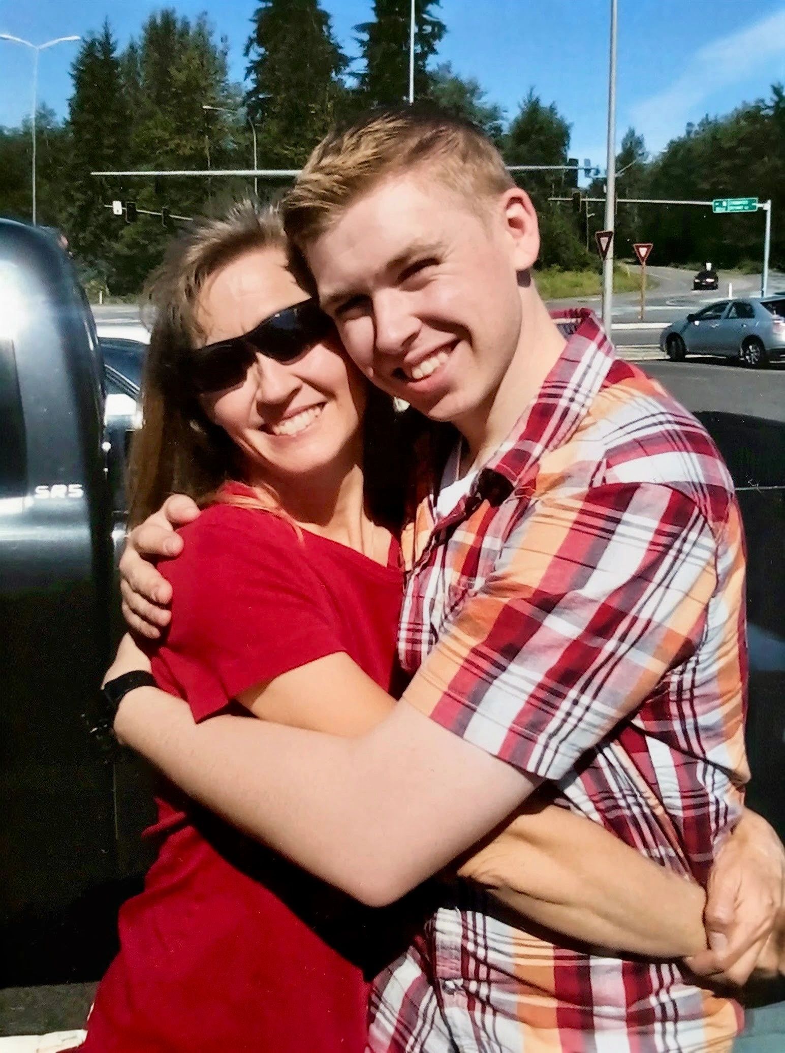 Two people smiling and hugging outdoors on a sunny day.