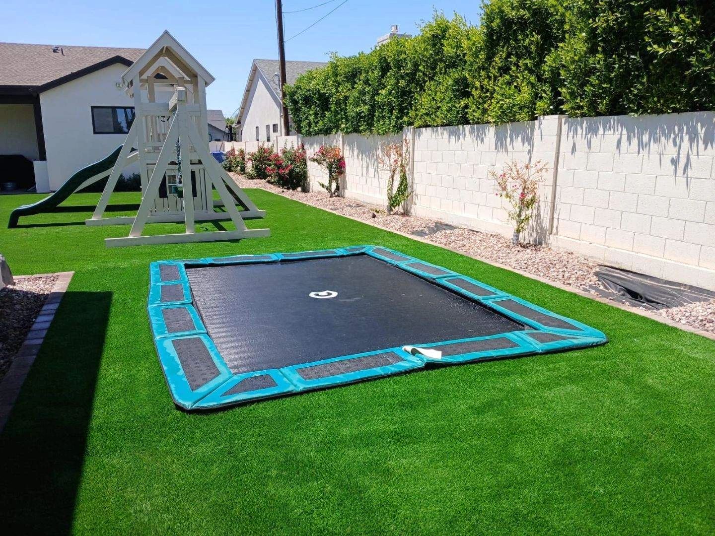 A backyard with a trampoline and a playset on green grass.