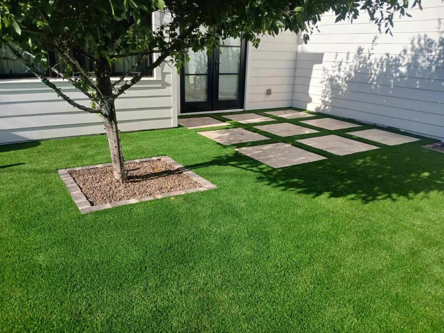 A green grassy backyard with stepping stones and a tree.