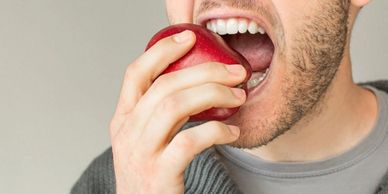 Man biting into a red apple, showing teeth and hand.