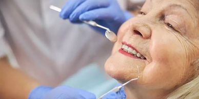 Dentist examining an elderly woman's teeth with dental tools.
