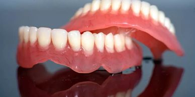 A set of upper and lower dentures on a reflective surface.