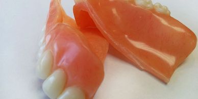 A pair of partial dentures with artificial teeth and pink gum base.