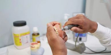 Dental technician shaping a dental prosthesis with a rotary tool.