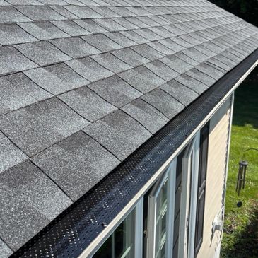 Close-up of a roof with asphalt shingles and a gutter guard installed.