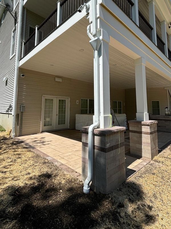 Covered patio area with tiled floor and white pillars under a house balcony.