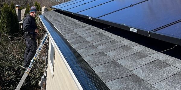 A person on a ladder working near solar panels on a rooftop.