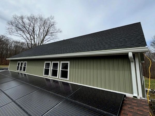 Solar panels installed on the roof of a green house with black shingles.