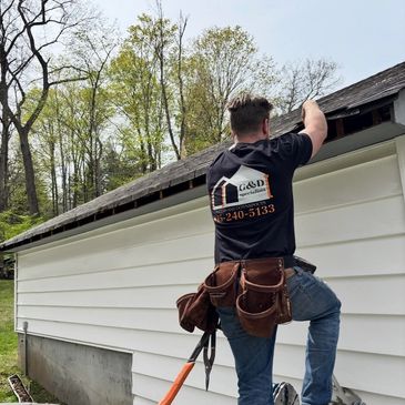 Worker inspecting or repairing house roof gutter on a sunny day.