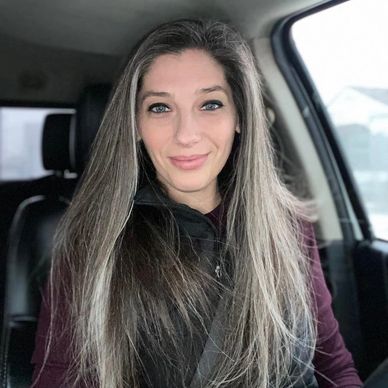Smiling woman with long hair in a car wearing a seatbelt.