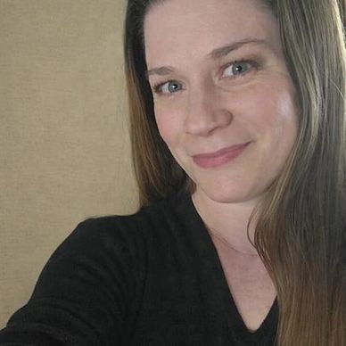 Woman with long hair smiling gently at the camera indoors.
