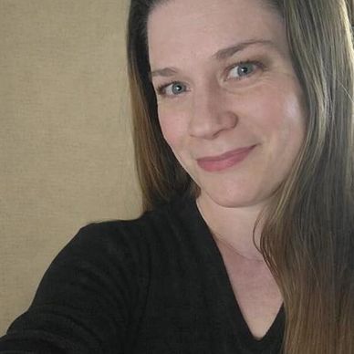 Woman with long hair smiling gently at the camera indoors.
