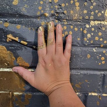Jess holding a paintbrush against a wall with gold and grey paint. 