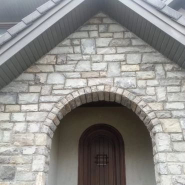 Stone archway entrance with wooden door beneath a gabled roof.