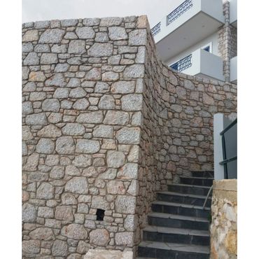 Stone wall with stairs leading up beside a modern building.