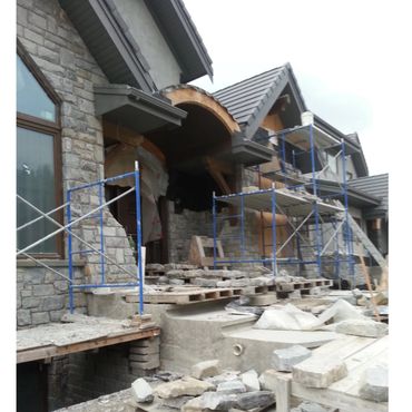 Stone house under construction with scaffolding and building materials.