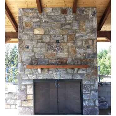 Stone fireplace with wooden mantle under a wooden roof.